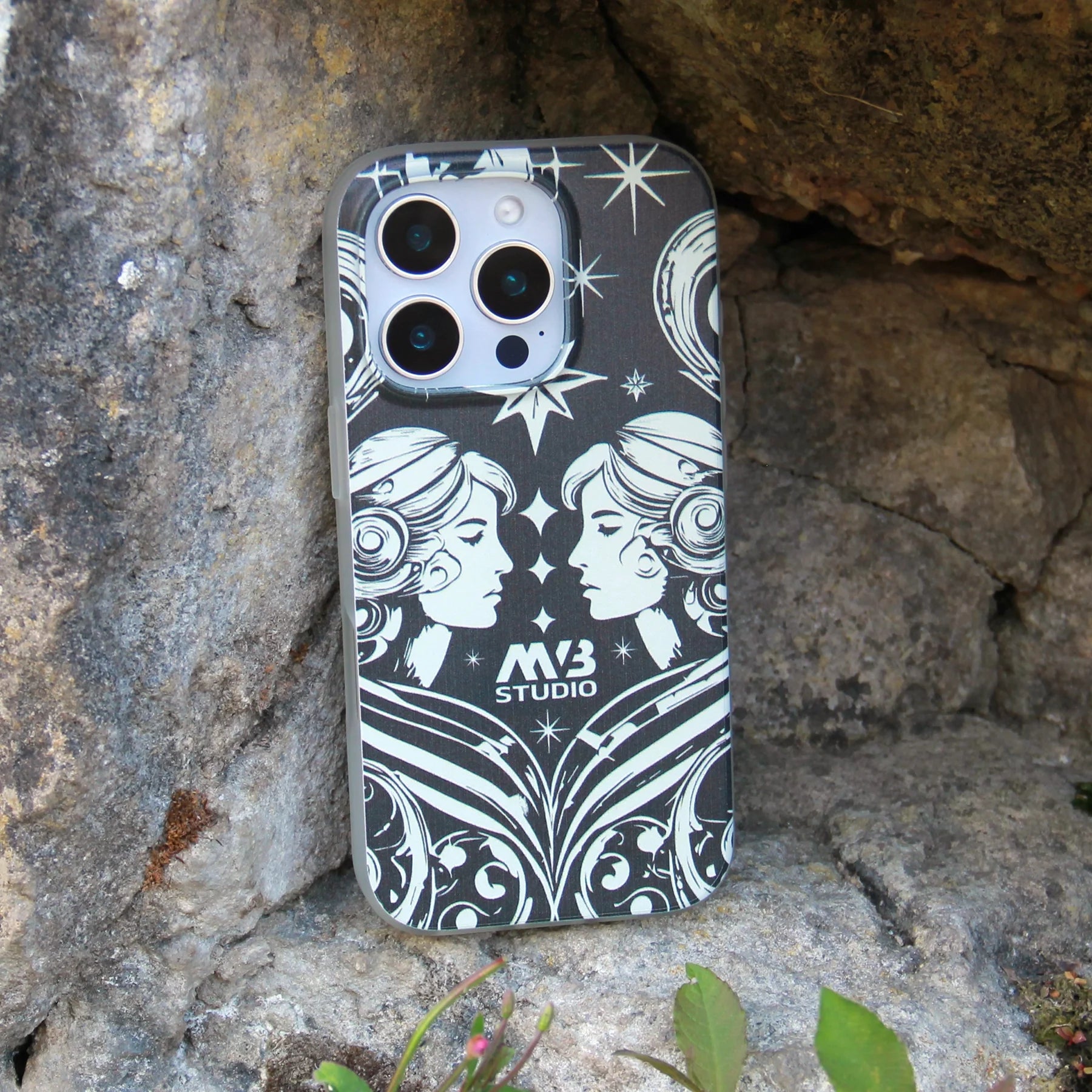 Stylish black and white iPhone case with 'MB Studio' logo, featuring Gemini zodiac-inspired or celestial art, on a rocky outdoor background