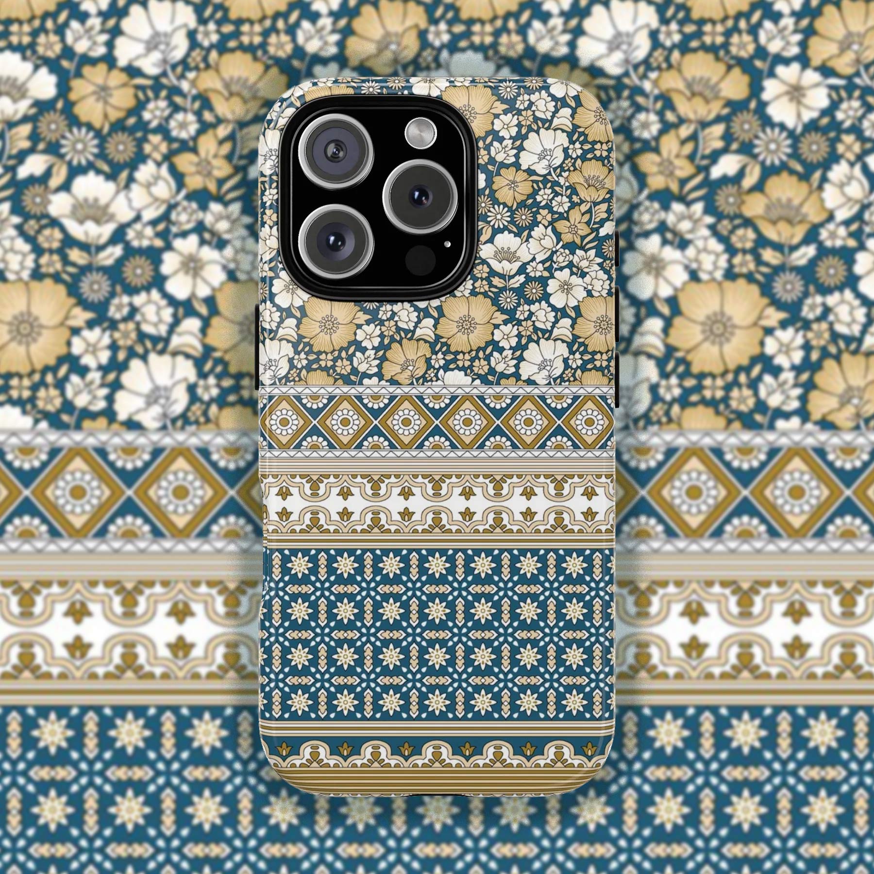 A phone case for an iPhone 15 Pro Max, showcasing a rich pattern with cream and gold florals at the top transitioning into horizontal bands of geometric patterns in blue, gold, and white, all against a matching patterned background.