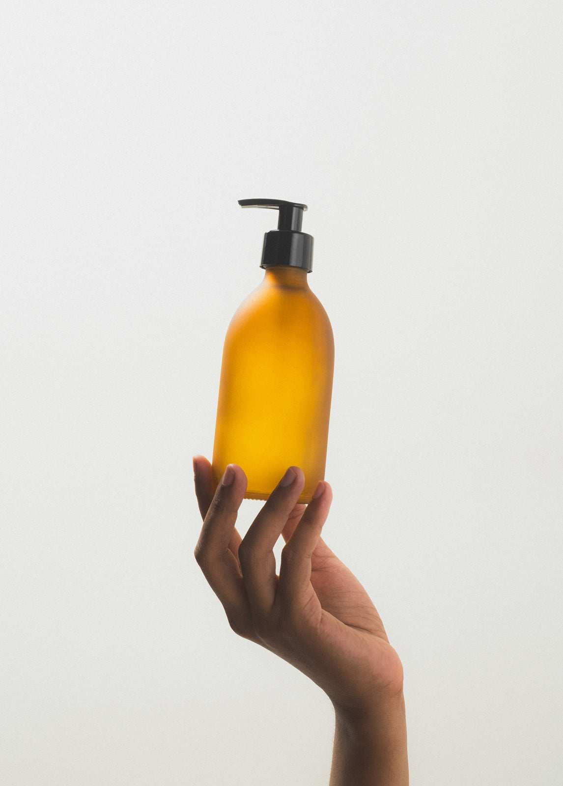 Hand holding a yellow bottle with a black pump against a light gray background