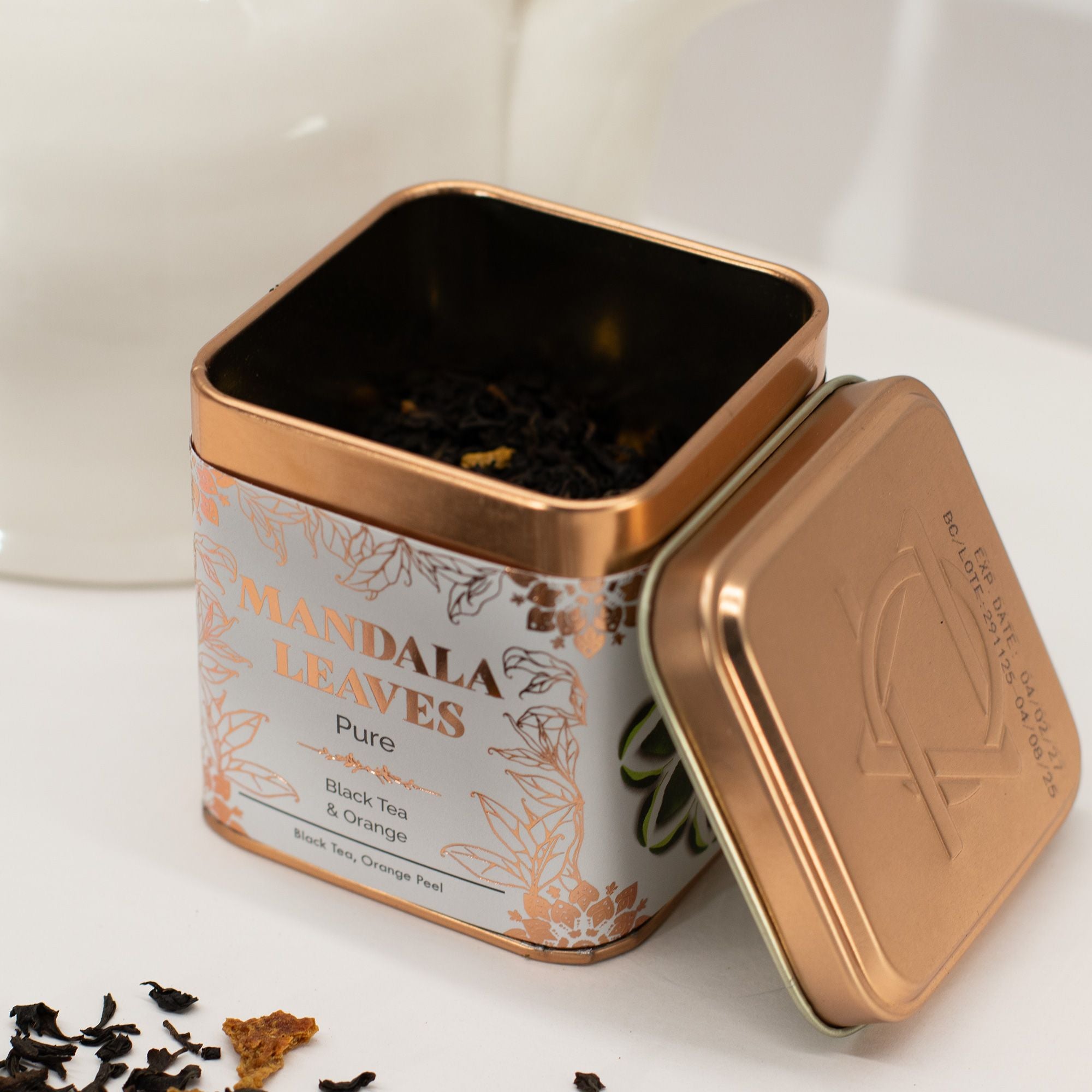 Tea canister labeled 'Mandala Leaves' with tea leaves spilling out on a white background