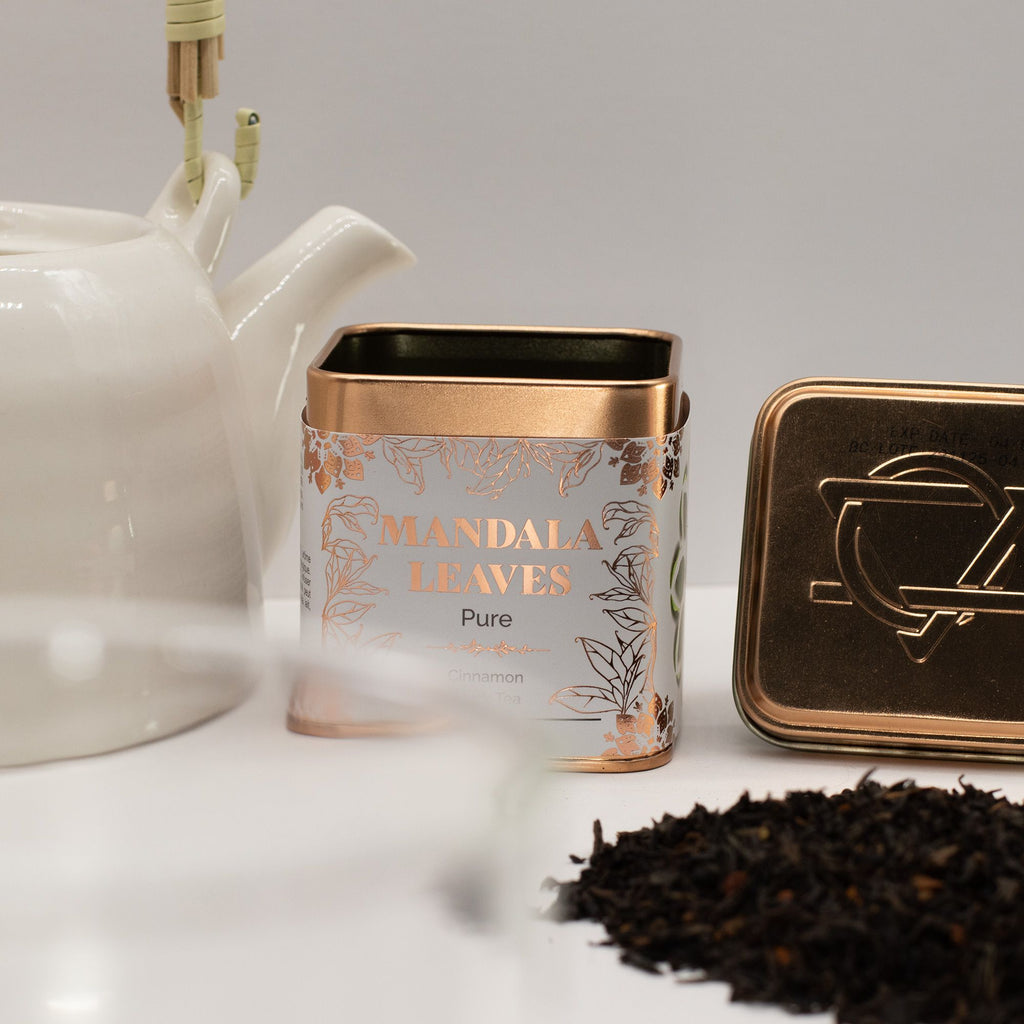 Tea canister labelled 'Mandala Leaves' Cinnamon Black Tea 50g with a teapot and tea leaves on a light surface.