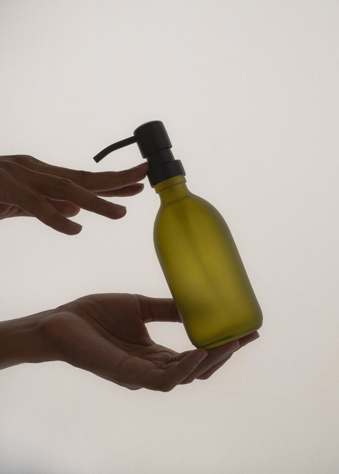 Person holding a green bottle with a black pump against a plain background