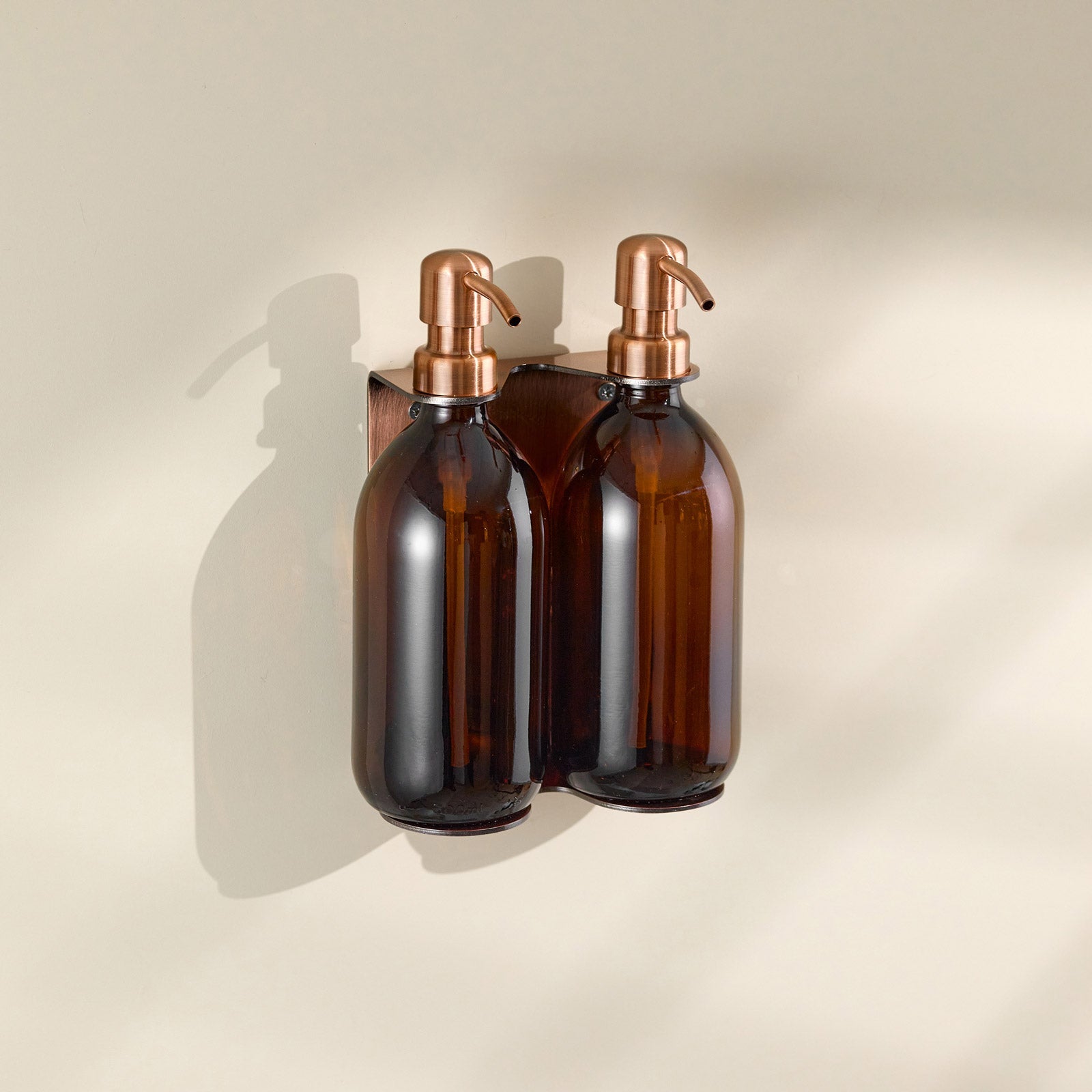 Two brown glass bottles with copper pumps on a beige background