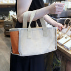 Person holding a beige tote bag with brown accents in a store setting