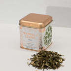 Tea tin labeled 'Mandala Leaves' with Ginger & Lemon Green Tea Sencha spilling out on a white background