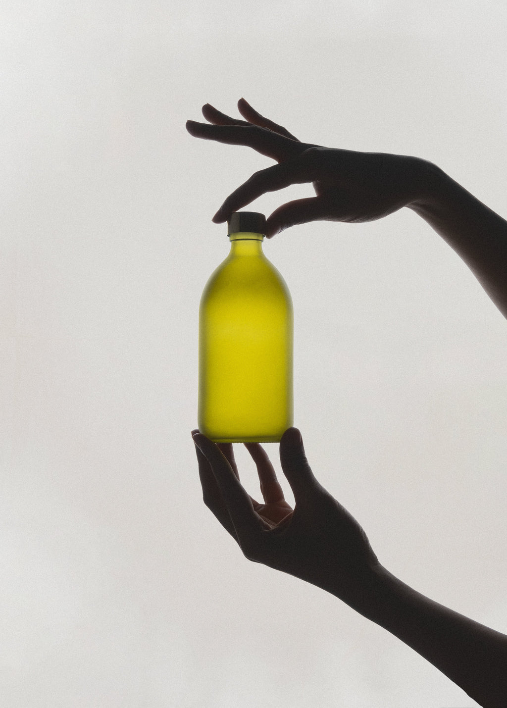 Silhouette of a hand holding a yellow bottle against a white background
