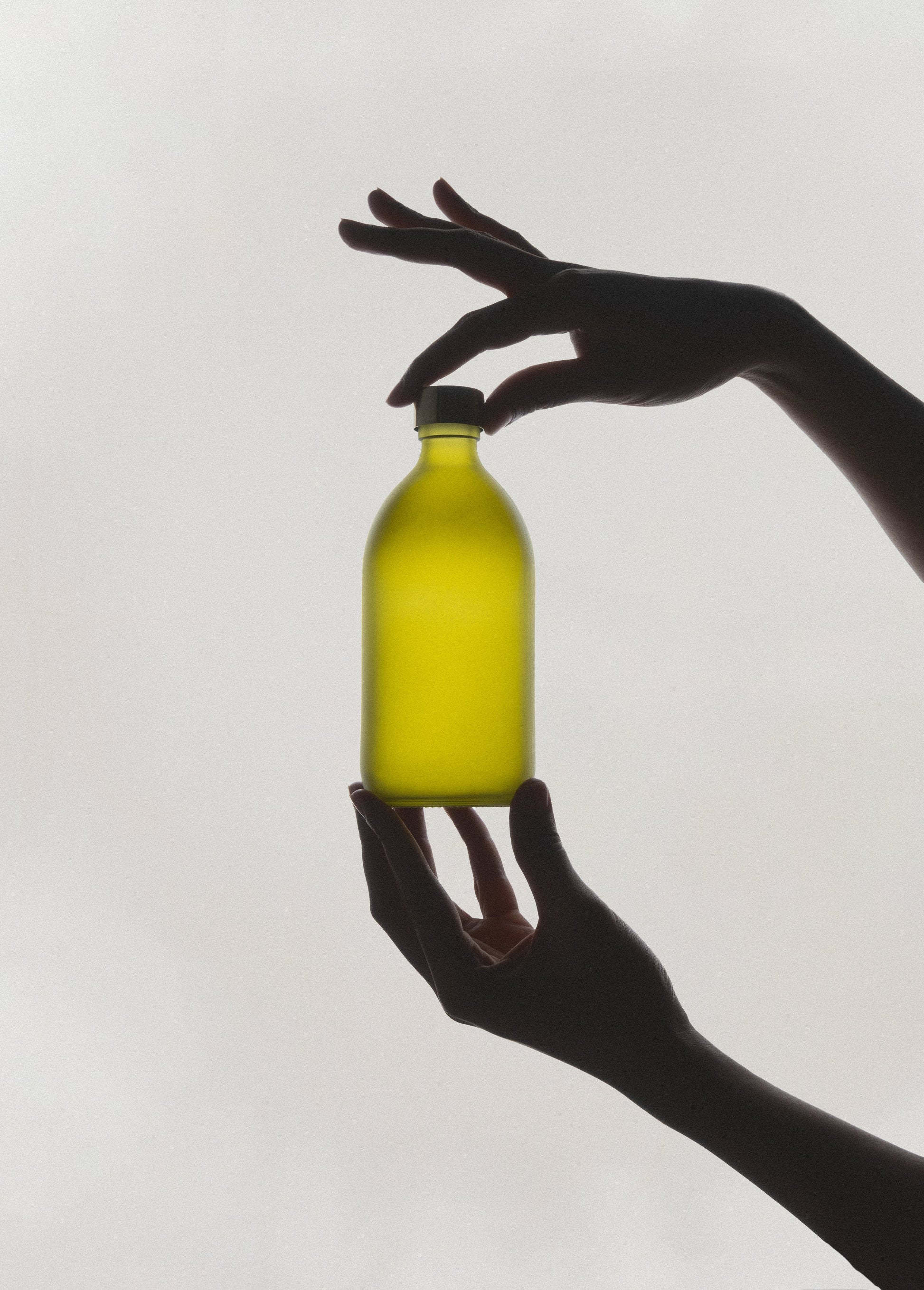 Silhouette of a hand holding a yellow bottle against a white background