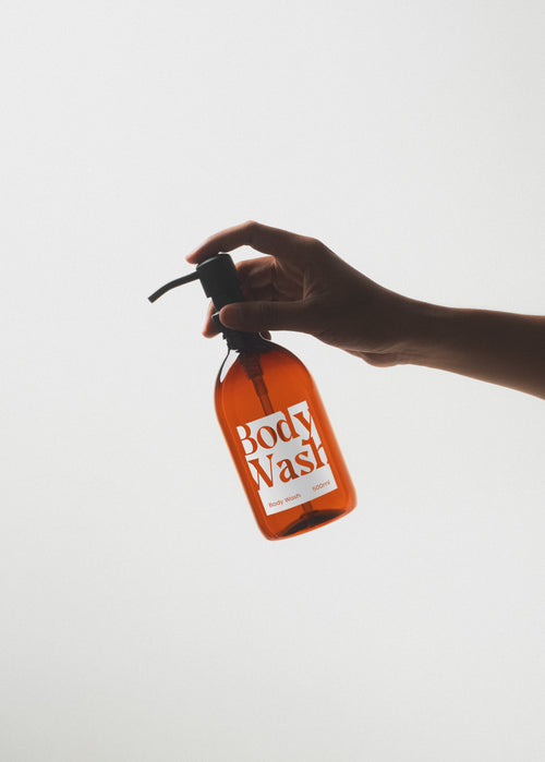 Hand holding an orange bottle of body wash against a white background