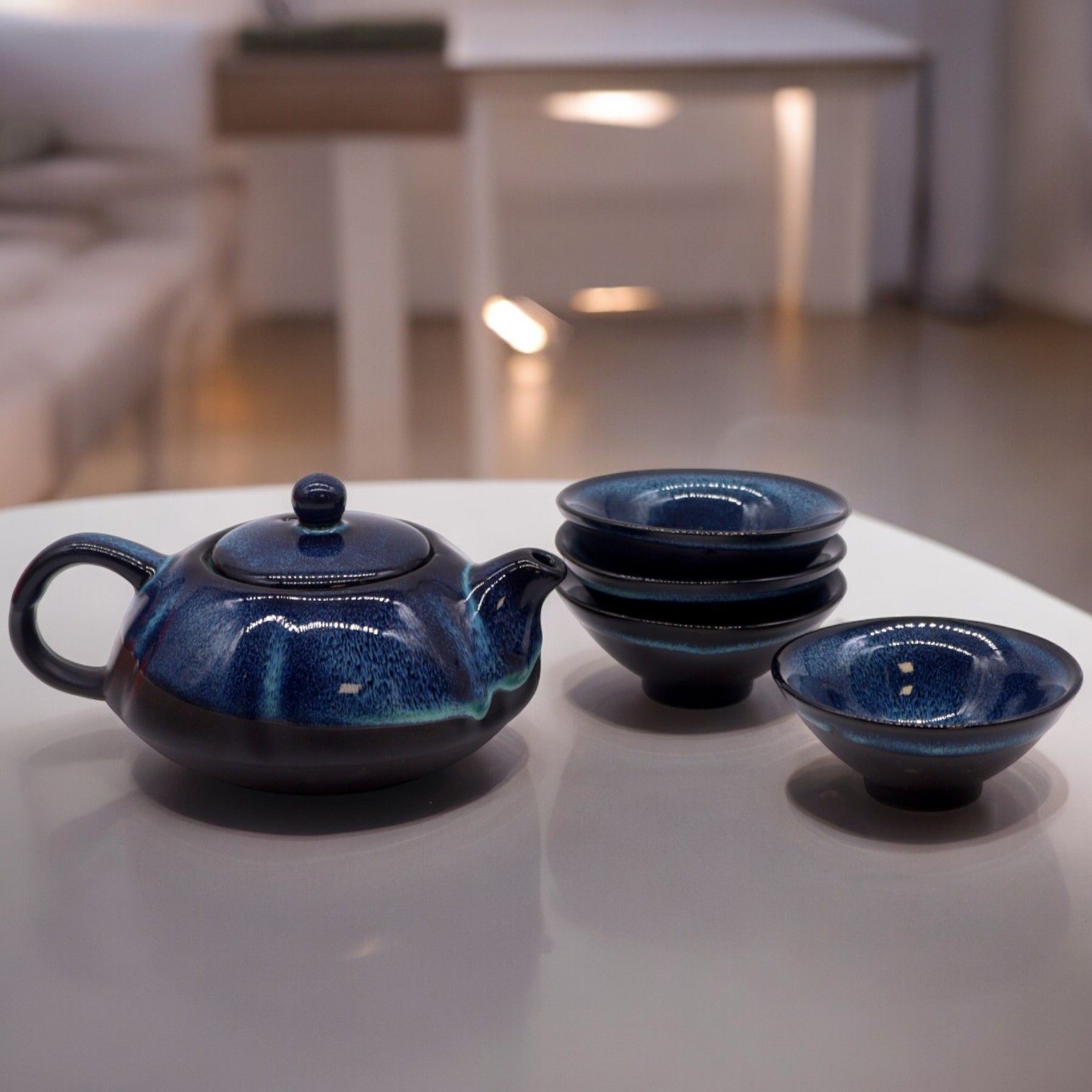 Blue ceramic teapot and four bowls on a white surface with a blurred indoor background