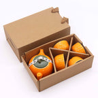 Ceramic orange-shaped containers with a green base in a cardboard box on a white background