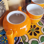 Orange teapot and cups on a colourful patterned tablecloth