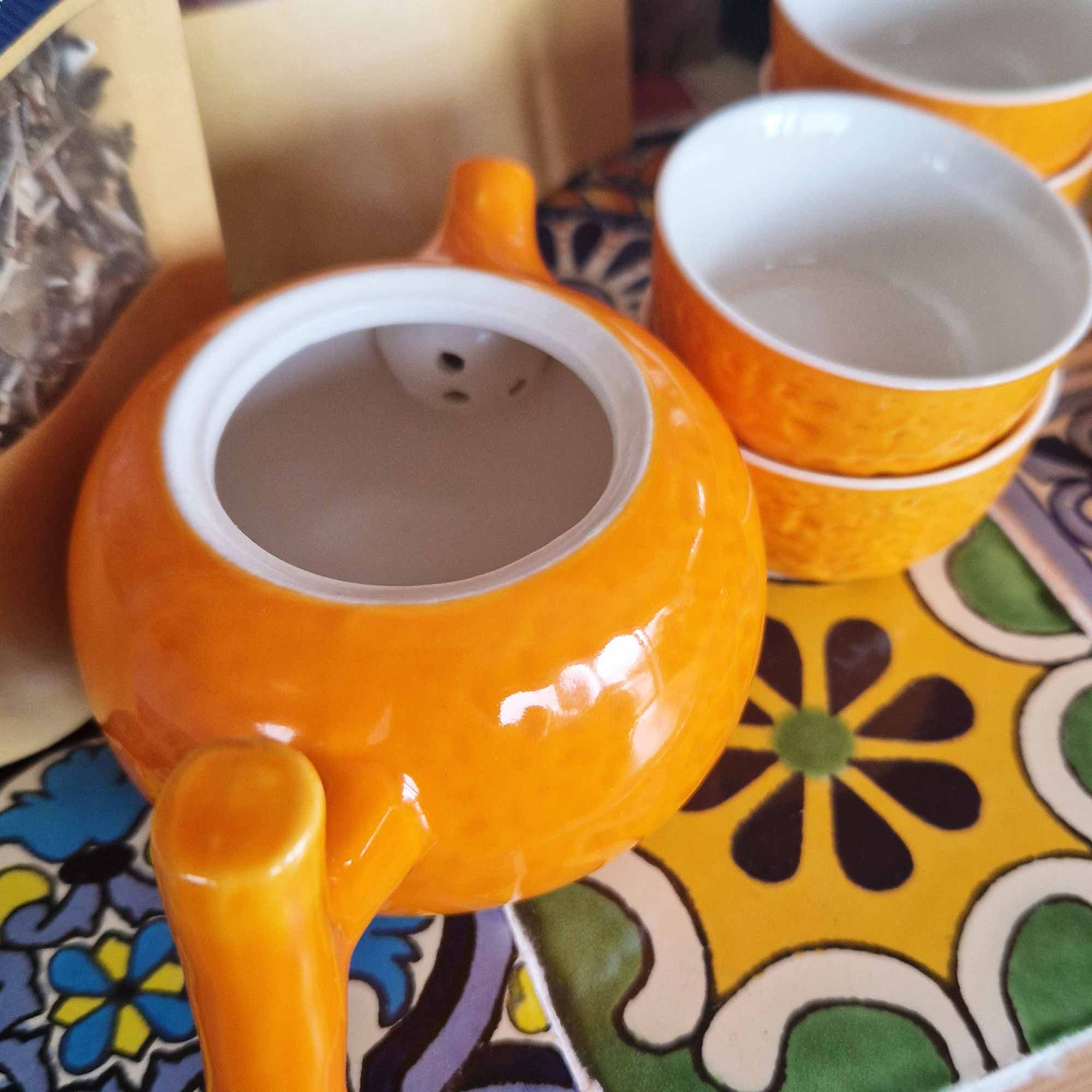 Orange teapot and cups on a colourful patterned tablecloth