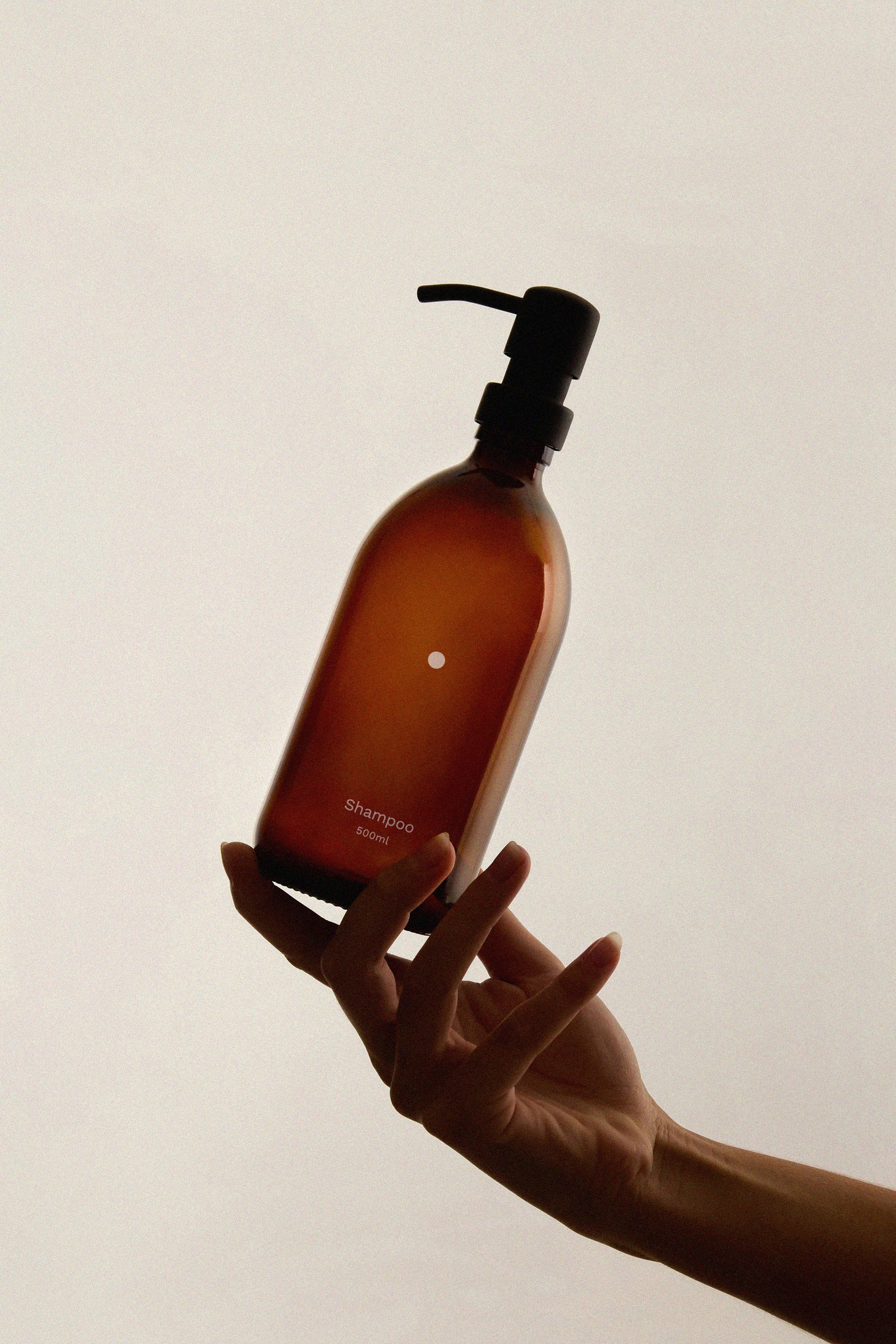 Hand holding a brown shampoo bottle with pump on a plain background