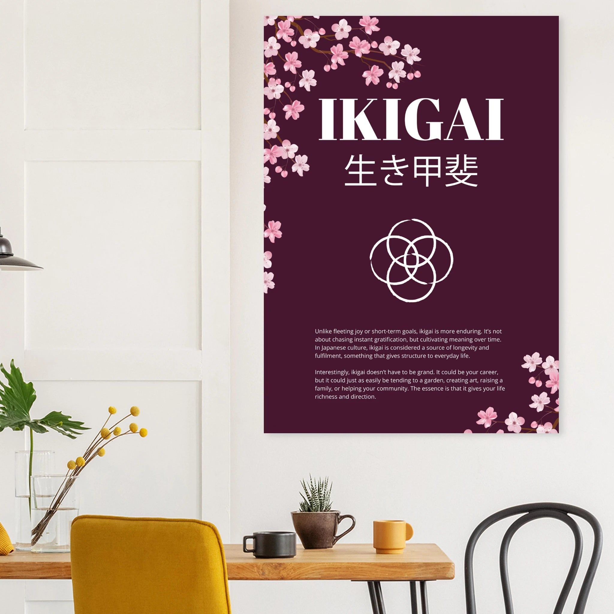 Wall poster titled “IKIGAI” with Japanese characters beneath, featuring cherry blossom illustrations on a deep burgundy background, displayed in a minimalist interior above a wooden table with plants and mugs.
