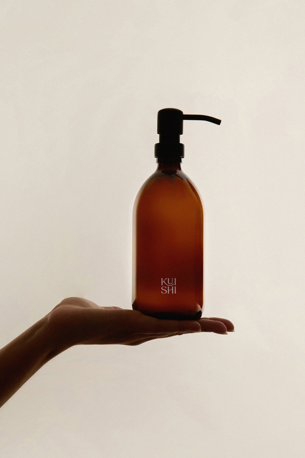 Amber bottle with pump dispenser held in a hand against a plain background