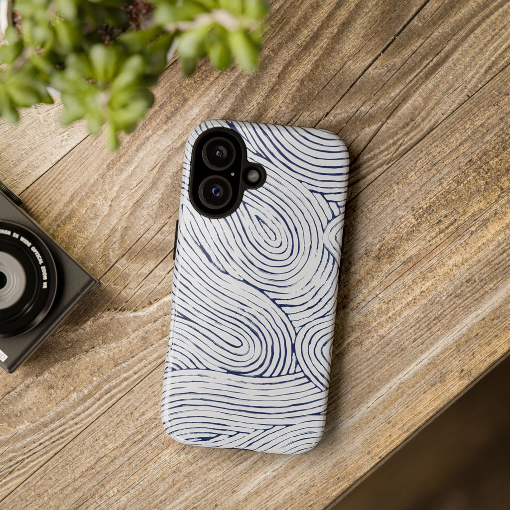 Indigo Flow Tough iPhone 16 Case with wavy pattern on a wooden surface next to a camera and plant