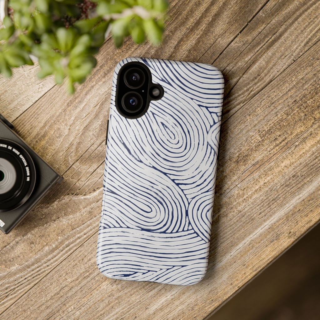 Indigo Flow Tough iPhone 16 Plus Case with wavy pattern on a wooden surface next to a camera and plant