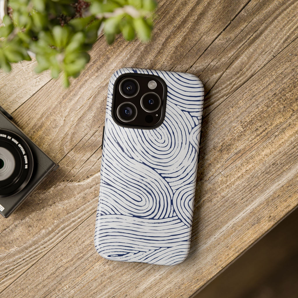 Indigo Flow Tough iPhone 16 Pro Case with wavy pattern on a wooden surface next to a camera and plant