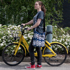Woman standing next to a yellow bicycle with a basket, wearing a blue patterned dress and red sneakers, in an outdoor setting with greenery and flowers.