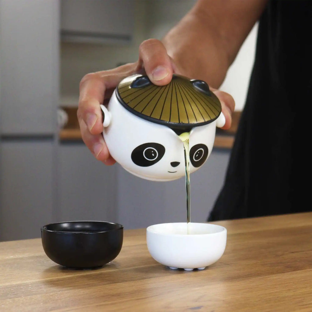 Tea infuser shaped like a panda pouring tea into a cup on a wooden table.