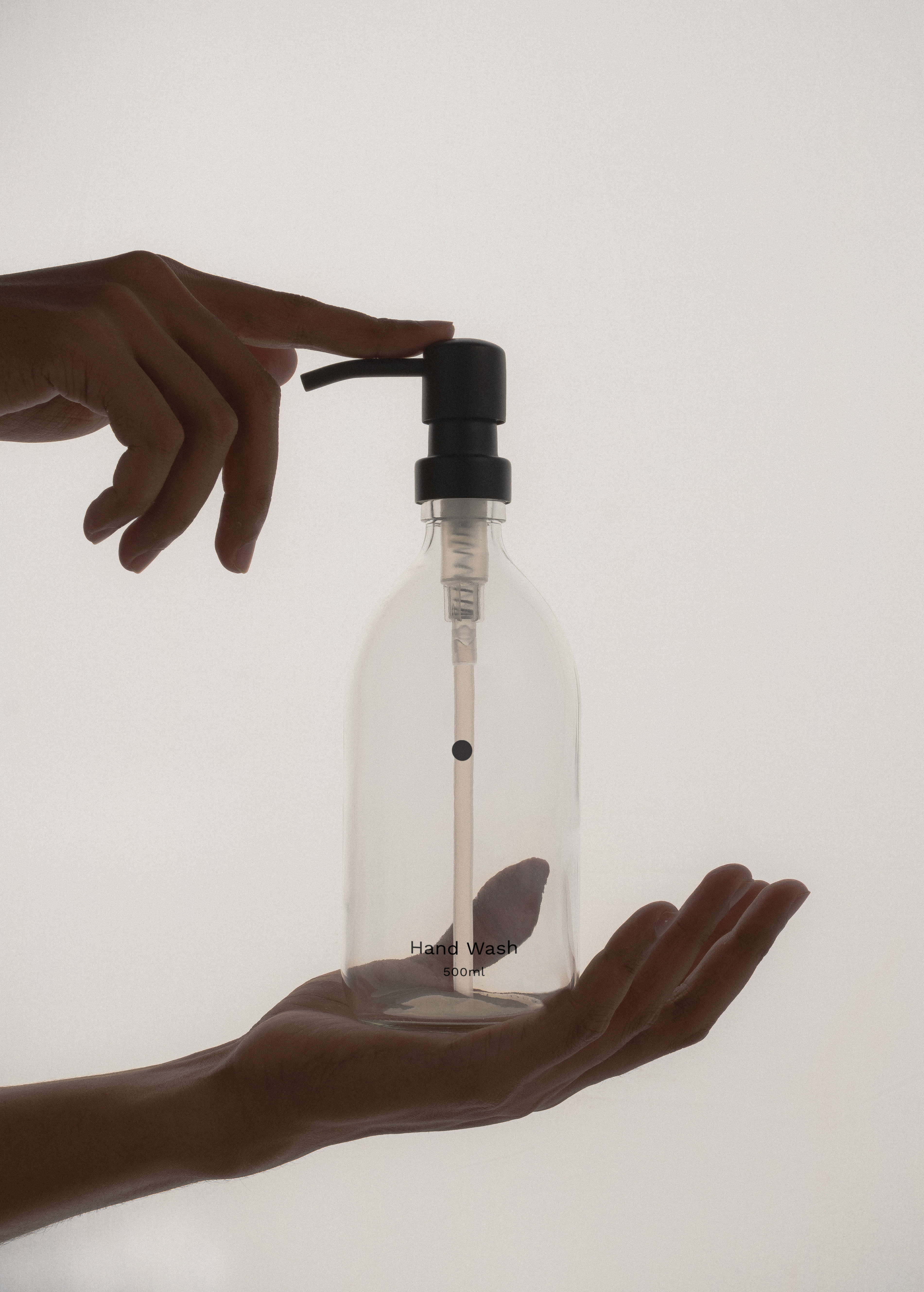 Clear glass bottle with black pump held by a hand on a white background