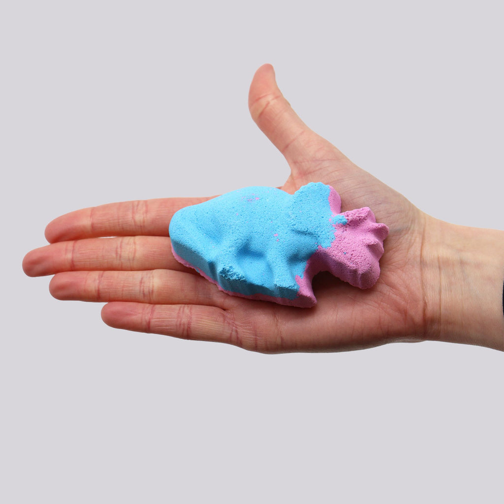 Hand holding a blue and pink bath bomb against a plain background