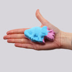 Hand holding a blue and pink bath bomb against a plain background