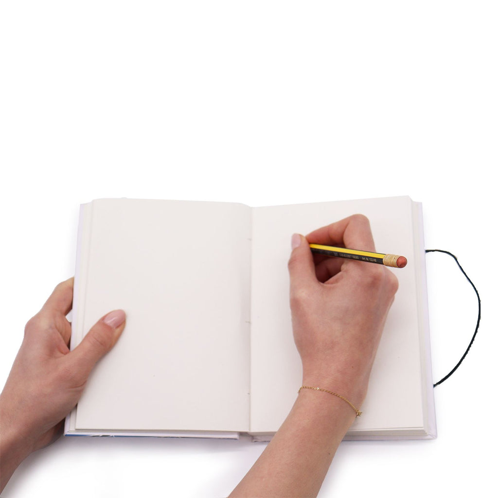 Person holding a pencil over an open notebook on a white background
