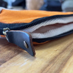 Close-up of a zipper on an orange and blue pouch with a wooden surface in the background.