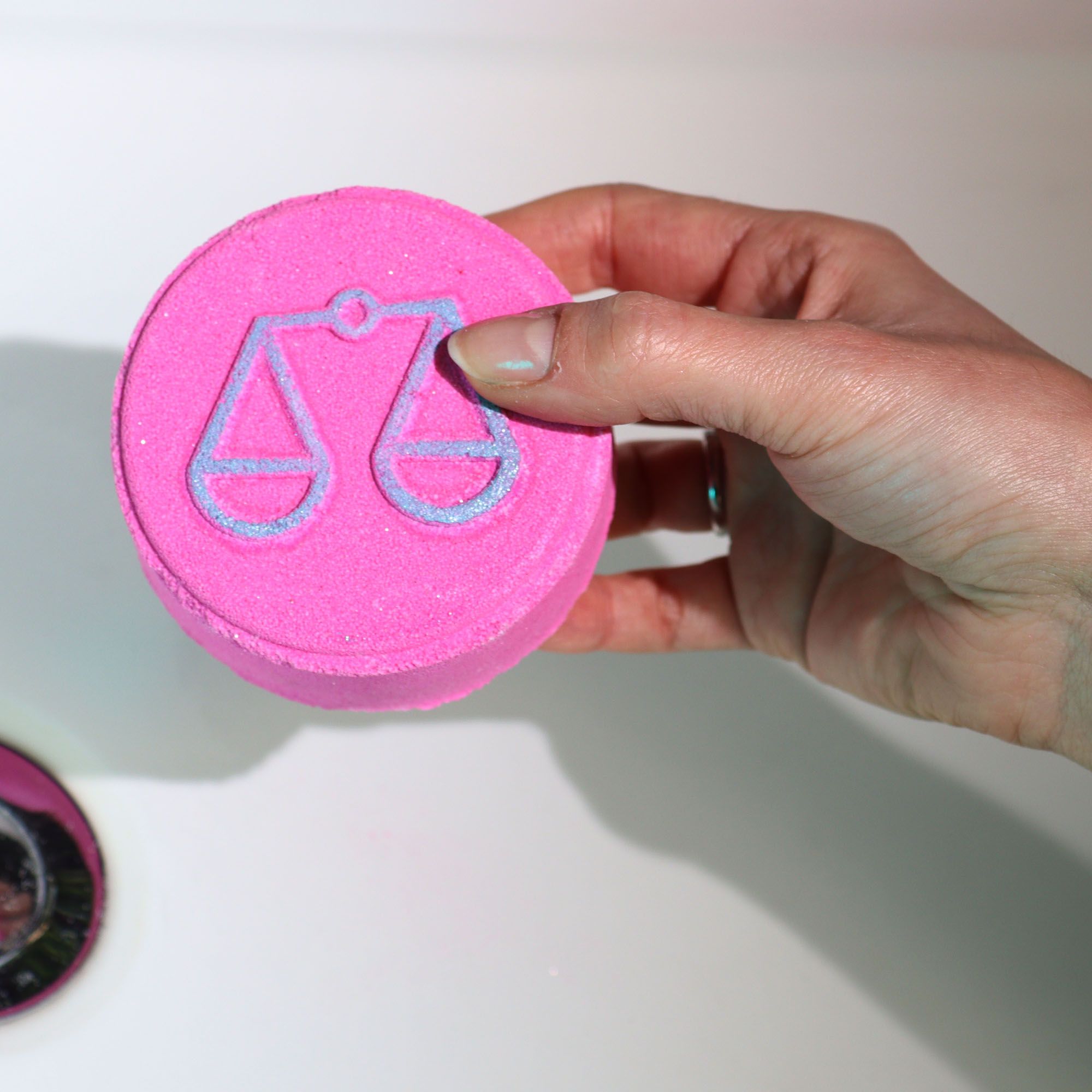 Hand holding a pink round object with a blue symbol on a white background