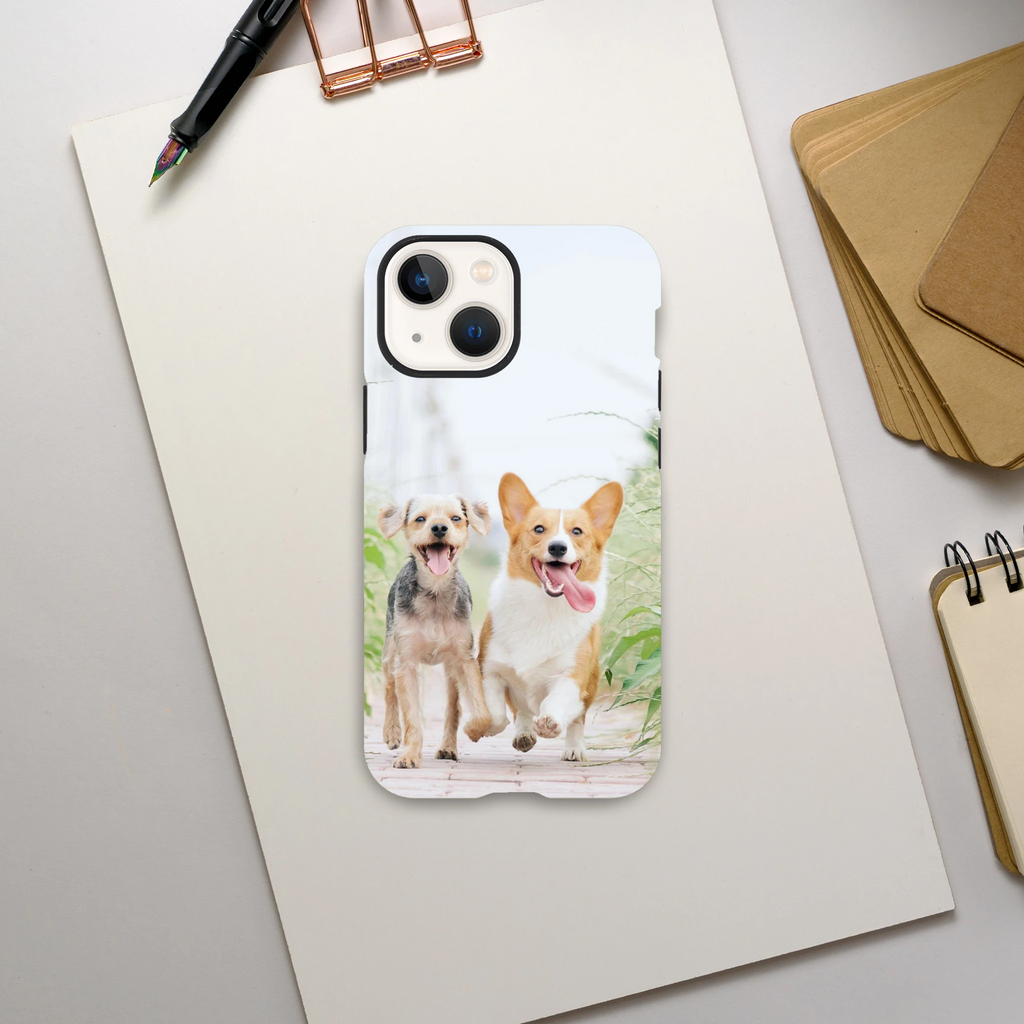 Personalised Photo Tough Case iPhone 13 Mini with two dogs on a white background, placed on a light gray surface with office supplies.