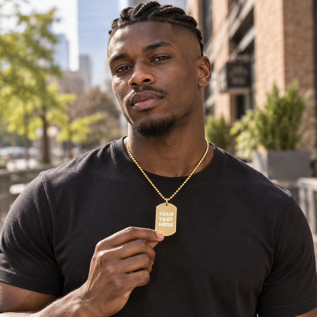 A man wearing a black t-shirt and a gold chain necklace with a gold dog tag pendant that reads 'YOUR TEXT HERE', set against an outdoor urban background.