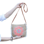 Hand holding a beige crossbody bag with colorful mandala design on a white background