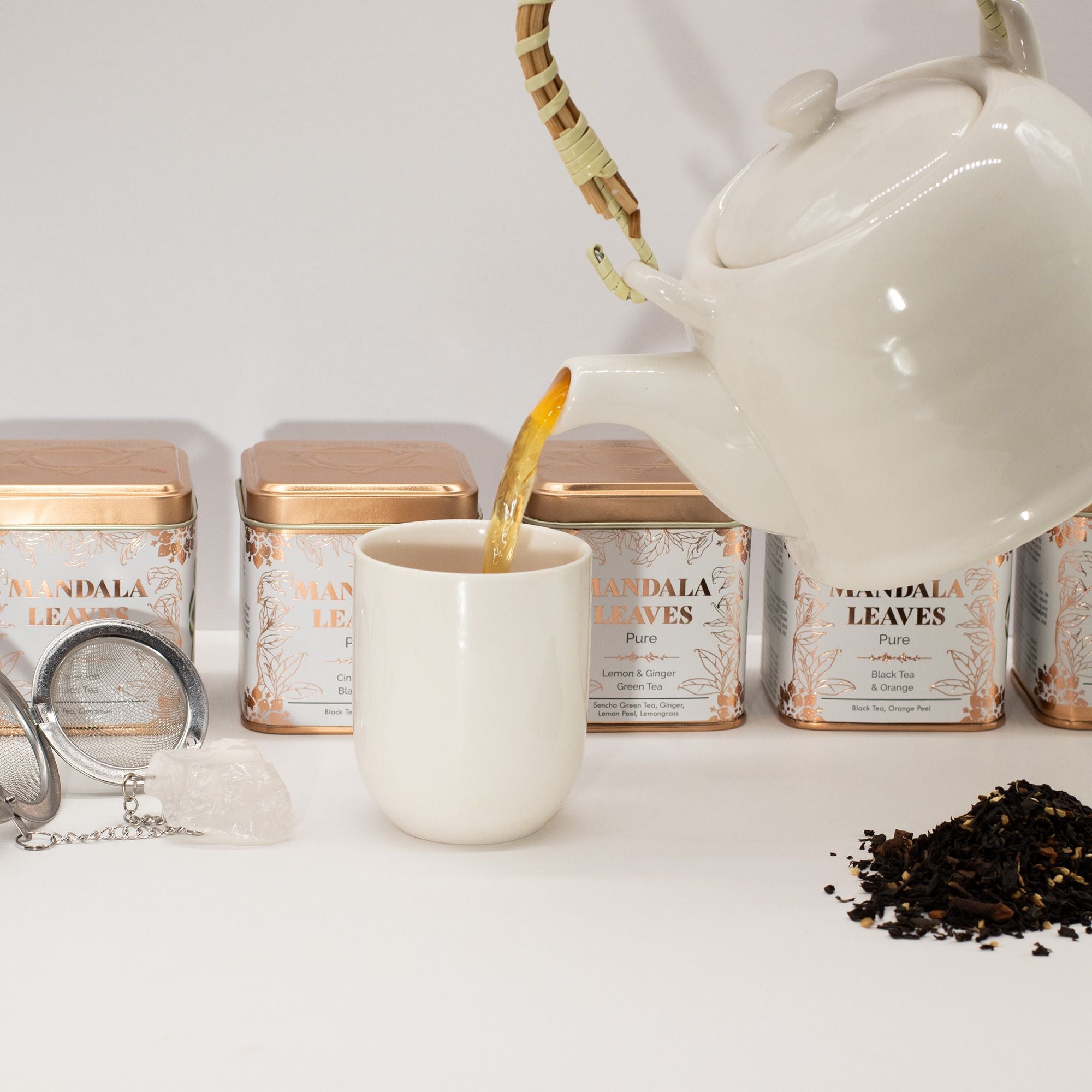 Ginger & Lemon Green Tea Sencha Blend being poured from a white teapot into a white mug with tea packaging in the background.
