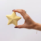 Hand holding a star-shaped yellow bath bomb against a light gray background