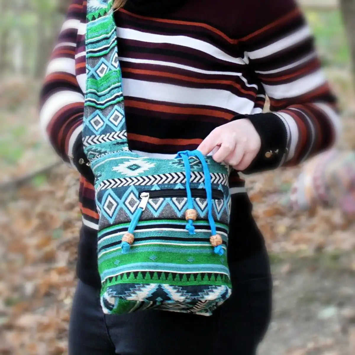 Person holding a colorful patterned Teal Sling Jacquard Bag with a blurred natural background