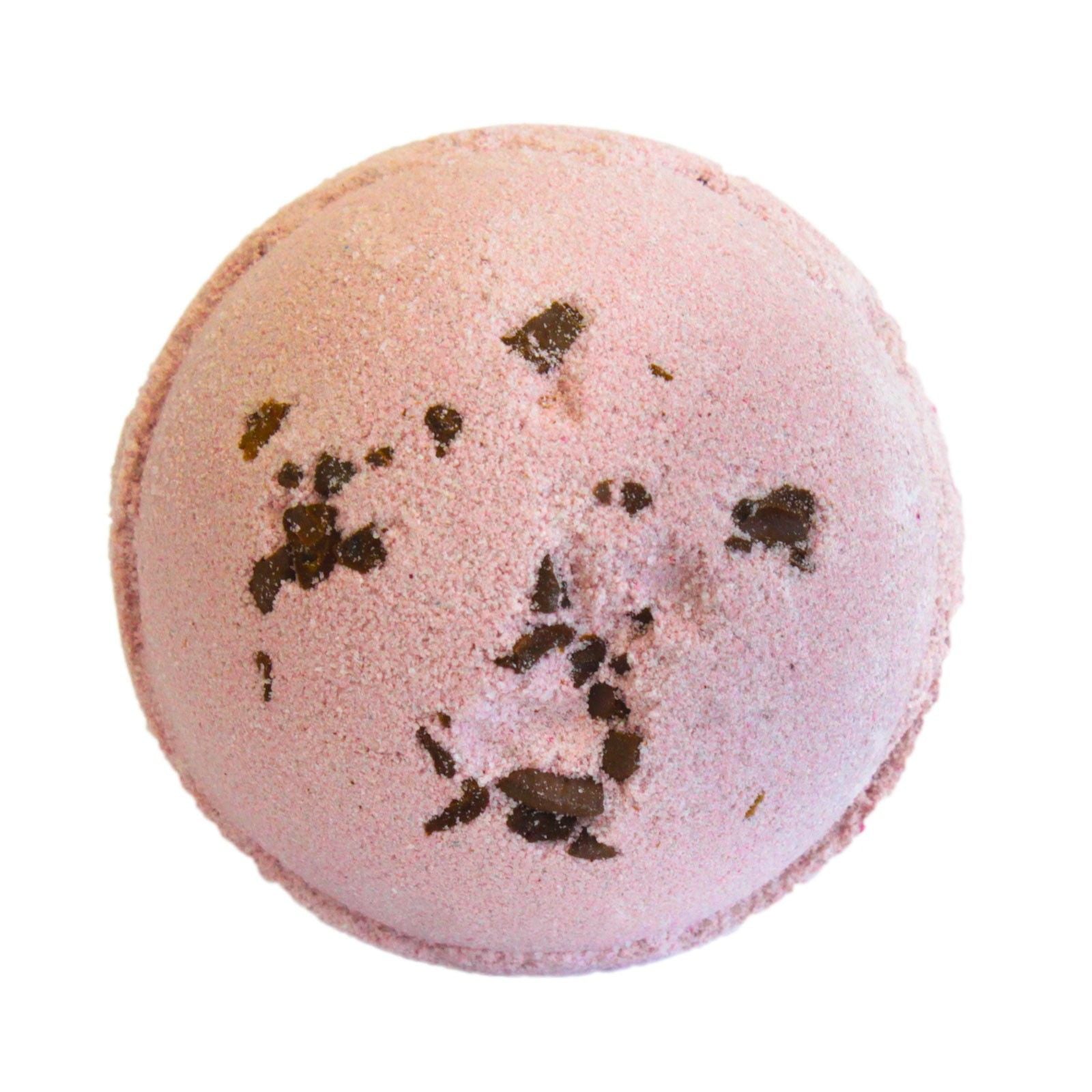 Pink bath bomb with dark specks on a white background