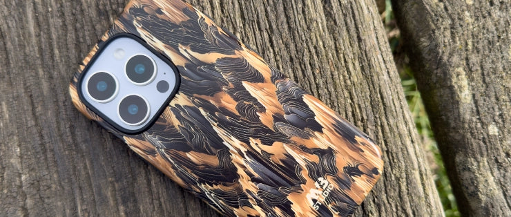 iPhone in a MVB Studio phone case with black, brown, and tan tones, resting on a weathered wooden bench outdoors