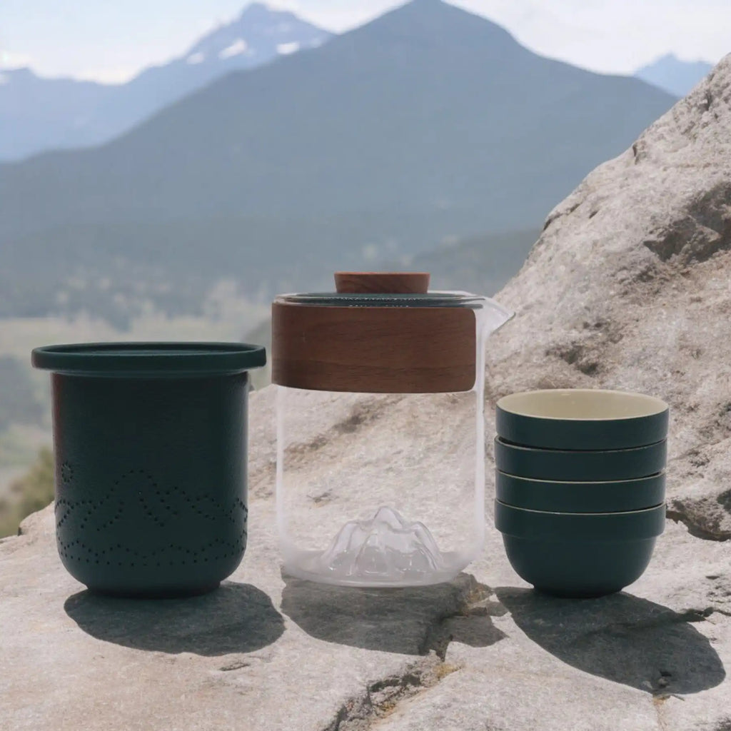 Travel Mountain Teapot Set with 4 Cups - Travel Pack on a rocky surface with mountains in the background.