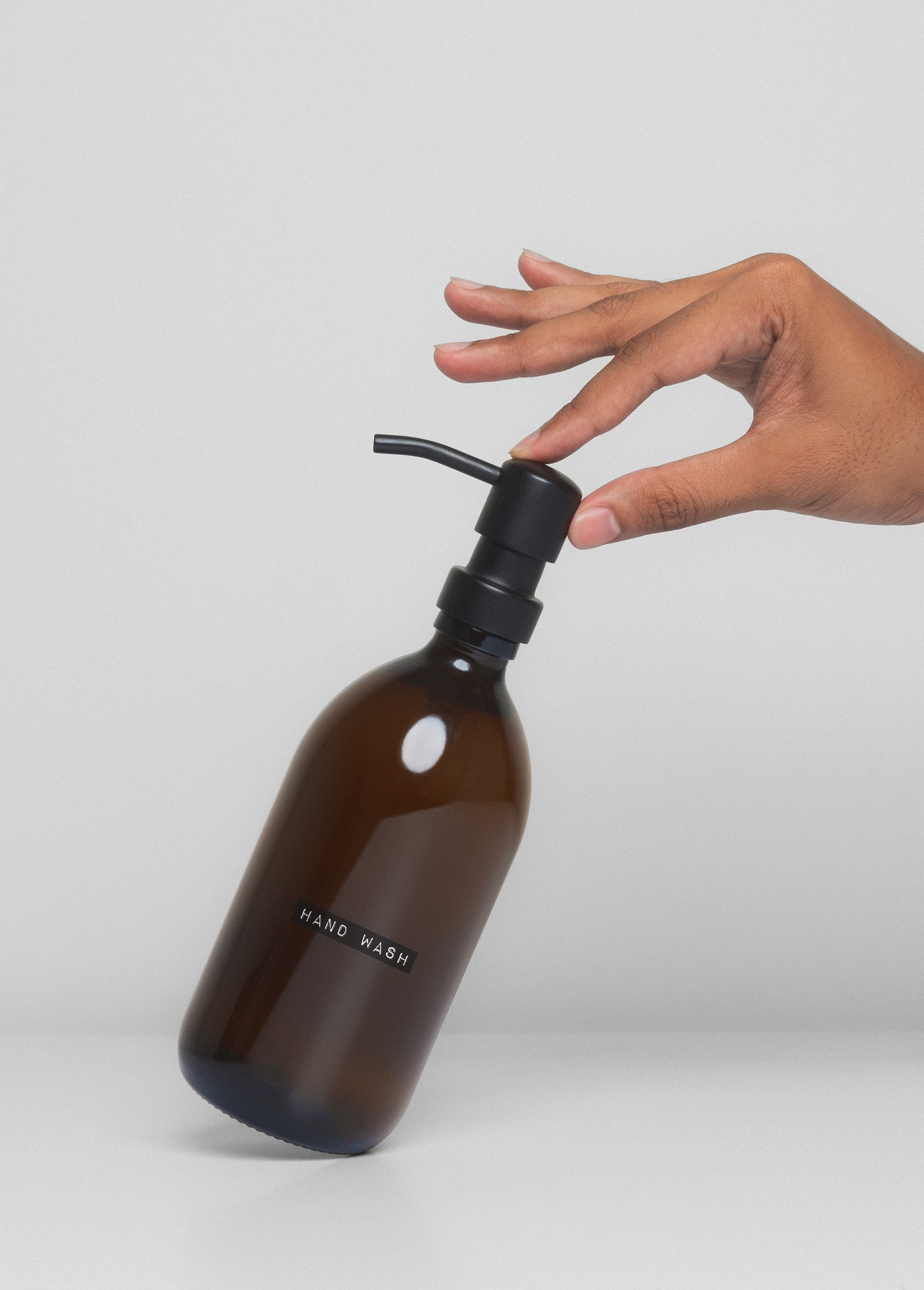 Brown hand wash bottle with black pump being held by a hand on a light gray background
