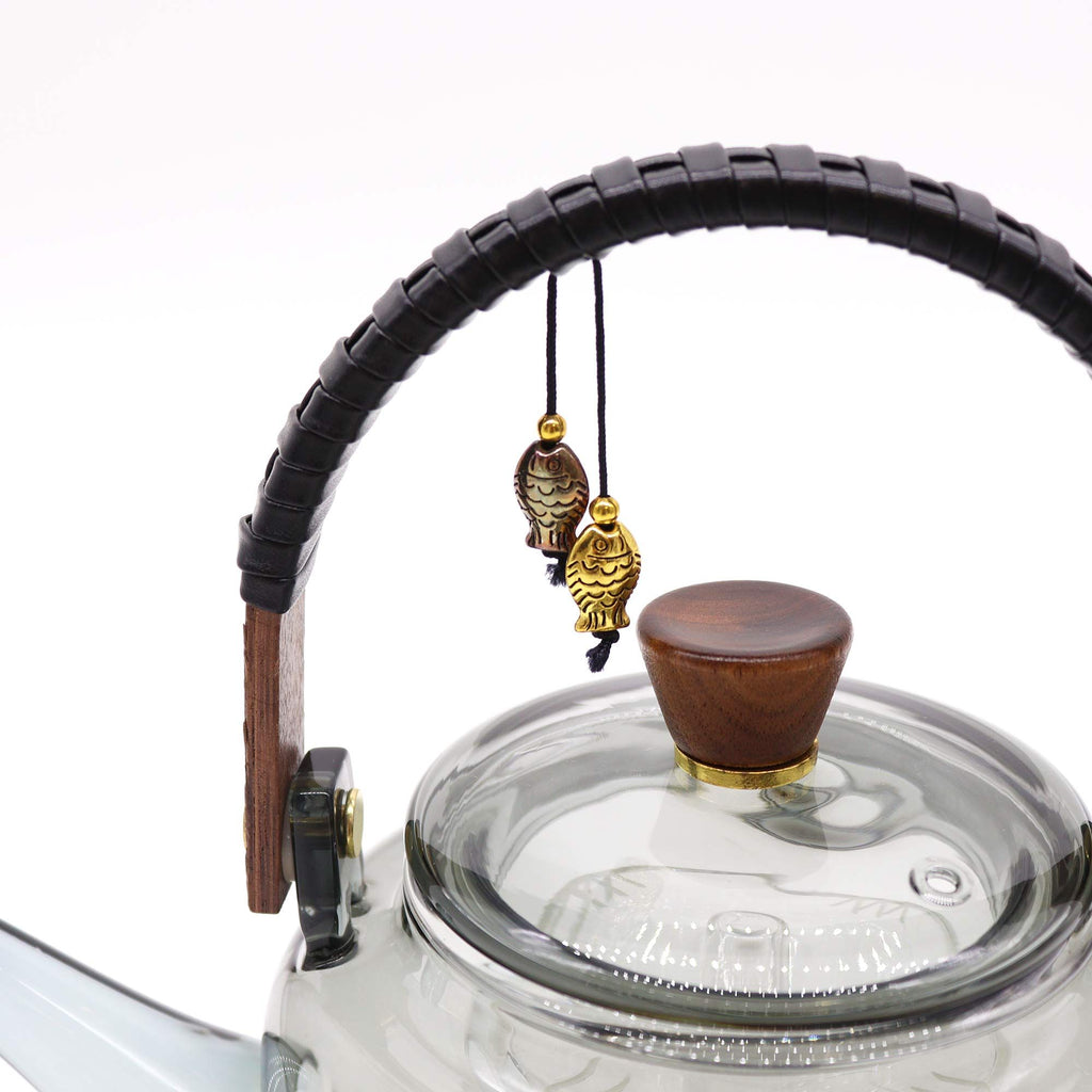 Glass teapot with wooden and black handle and lid knob on a white background