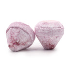 Close-up of two pink, faceted solid objects with a frosted, powdery surface on a white background, one upright and one resting on its side.