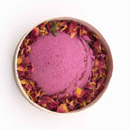 Pink bath bomb with floral petals in a white container on a white background