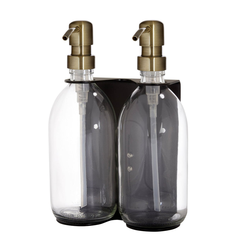 Two clear glass bottles with gold pumps in a black holder on a white background