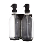 Two clear bottles with black pumps in a black holder on a white background