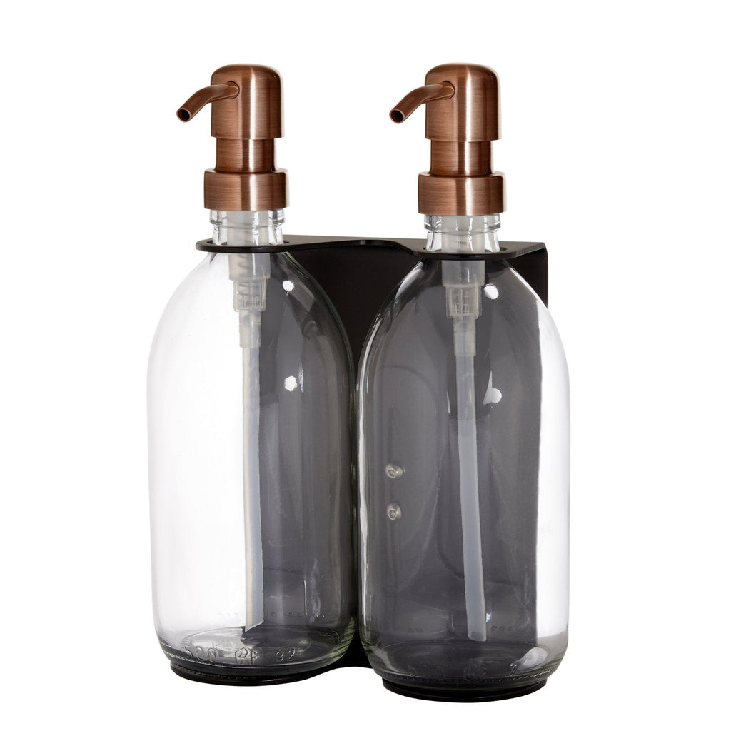 Two clear glass bottles with copper pumps in a black holder on a white background