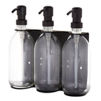 Three clear glass bottles with black pumps in a black holder on a white background