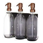 Three glass bottles with bronze pumps in a black holder on a white background