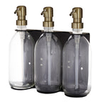 Three clear glass bottles with gold pumps in a black holder on a white background