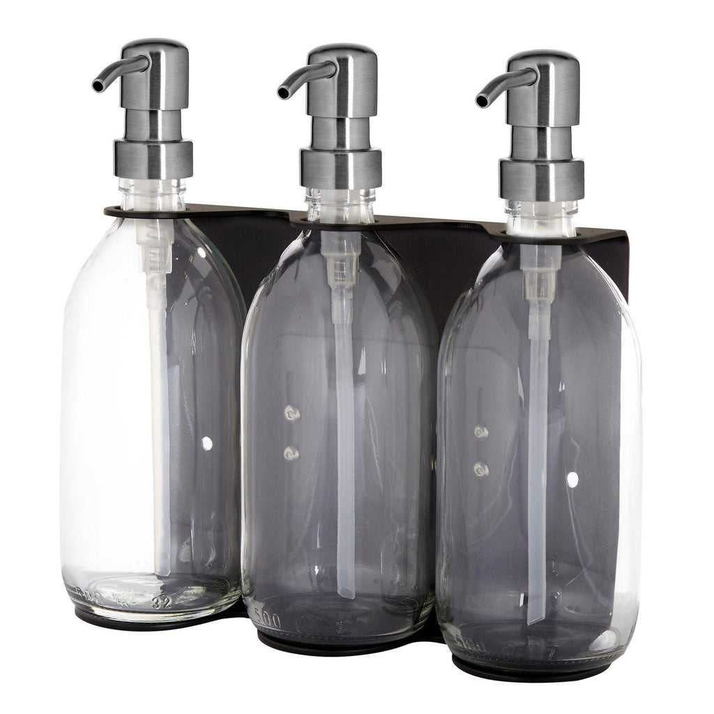 Set of three clear glass bottles with silver pumps in a black holder on a white background